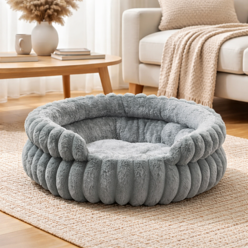 Beroligende rund hundeseng med høye kanter i grå plysj, plassert i stue